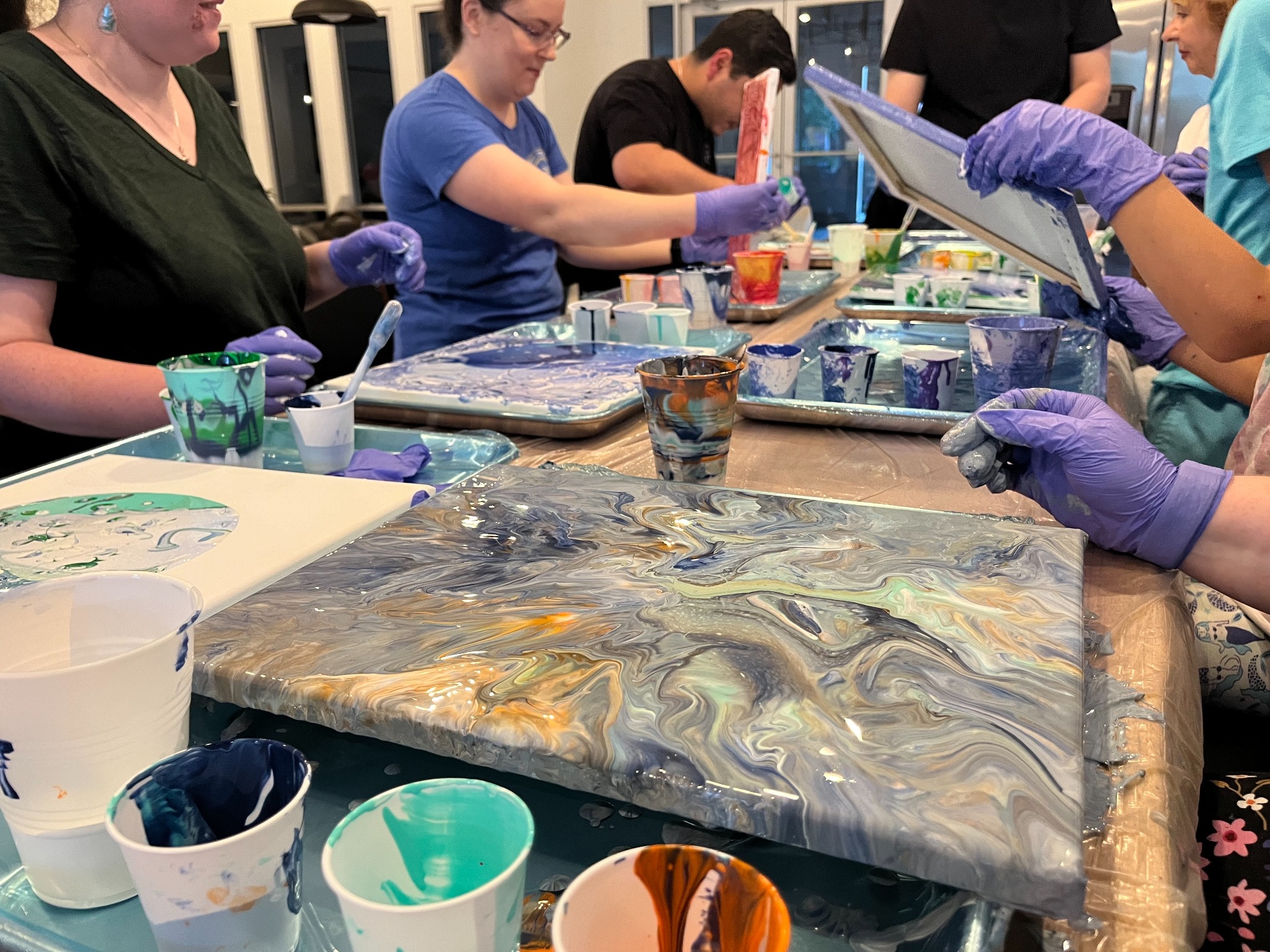 A group gathered around a table pouring fluid acrylic paint onto canvases